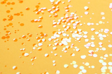 Photo of Shiny bright orange glitter on yellow background, closeup