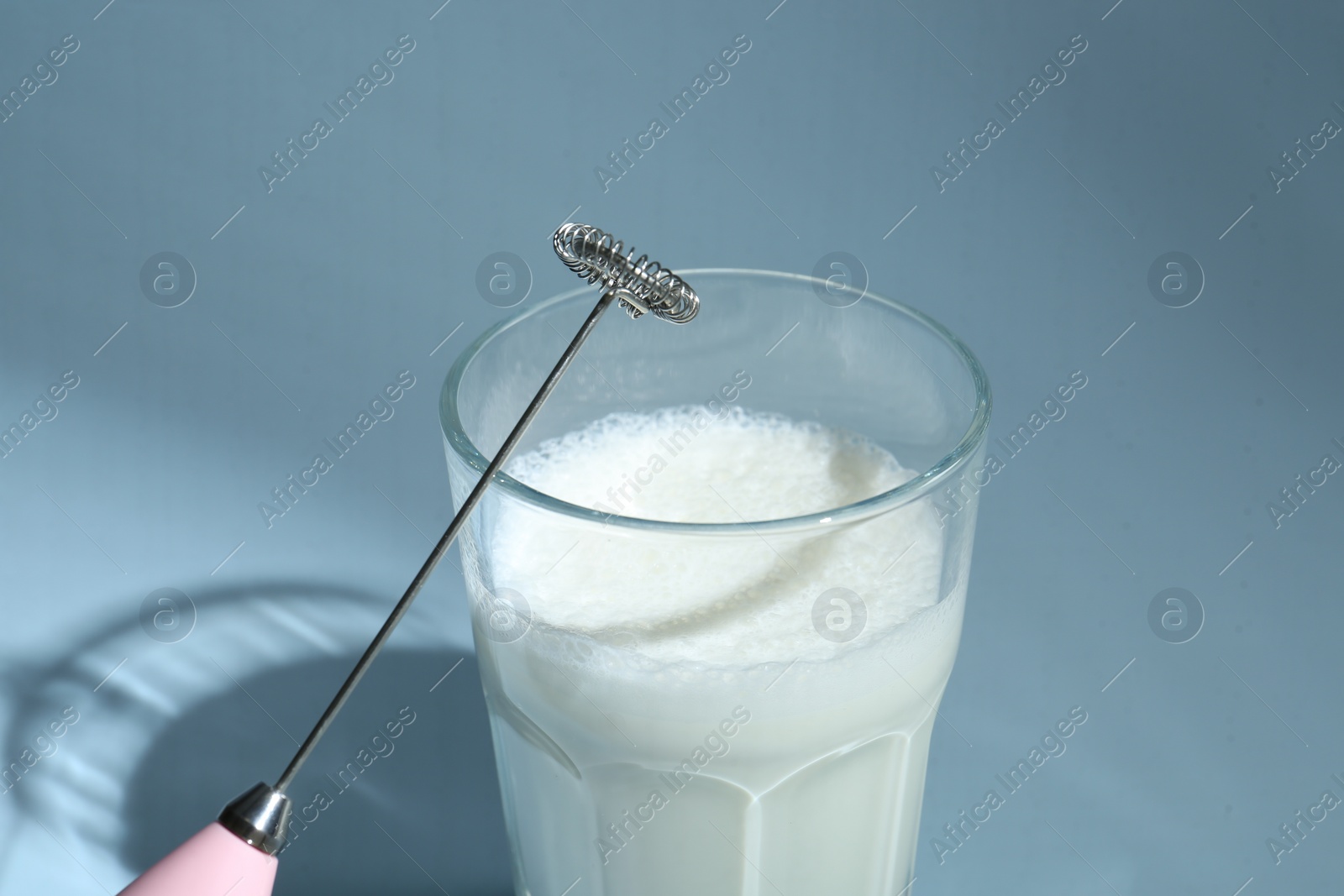 Photo of Mini mixer (milk frother) and whipped milk in glass on light blue background, closeup