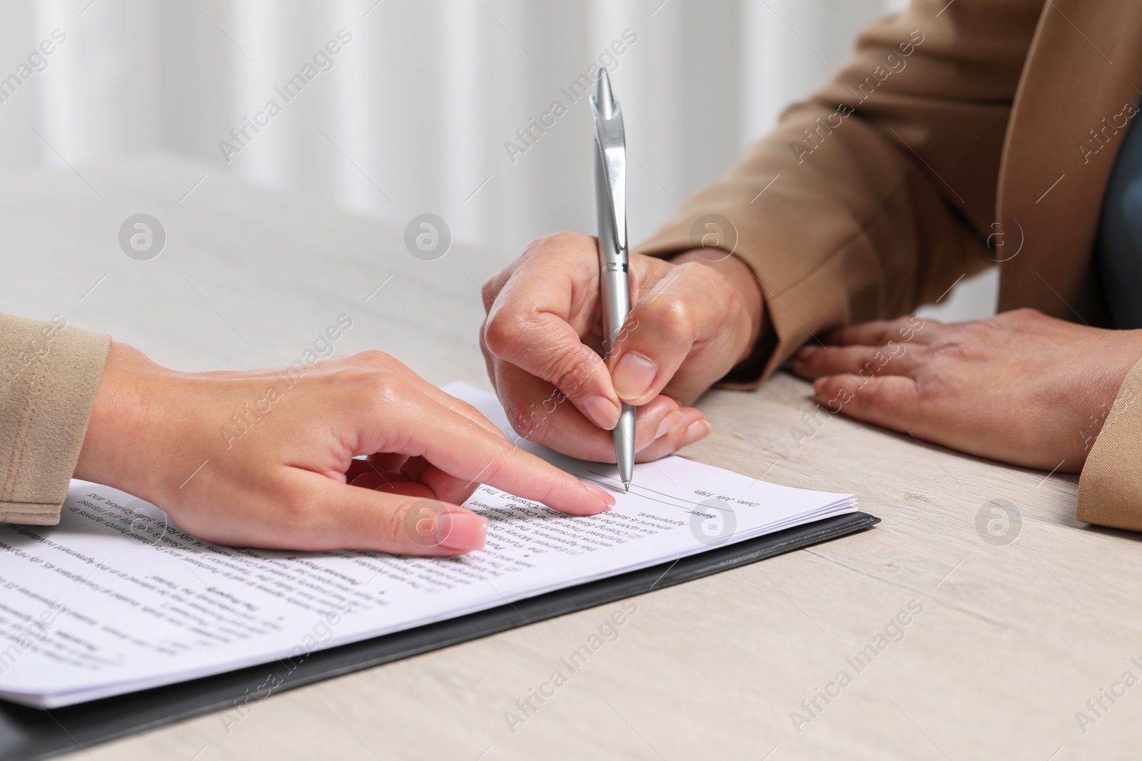 Photo of Manager showing client where she must to mark signature at light wooden table indoors, closeup