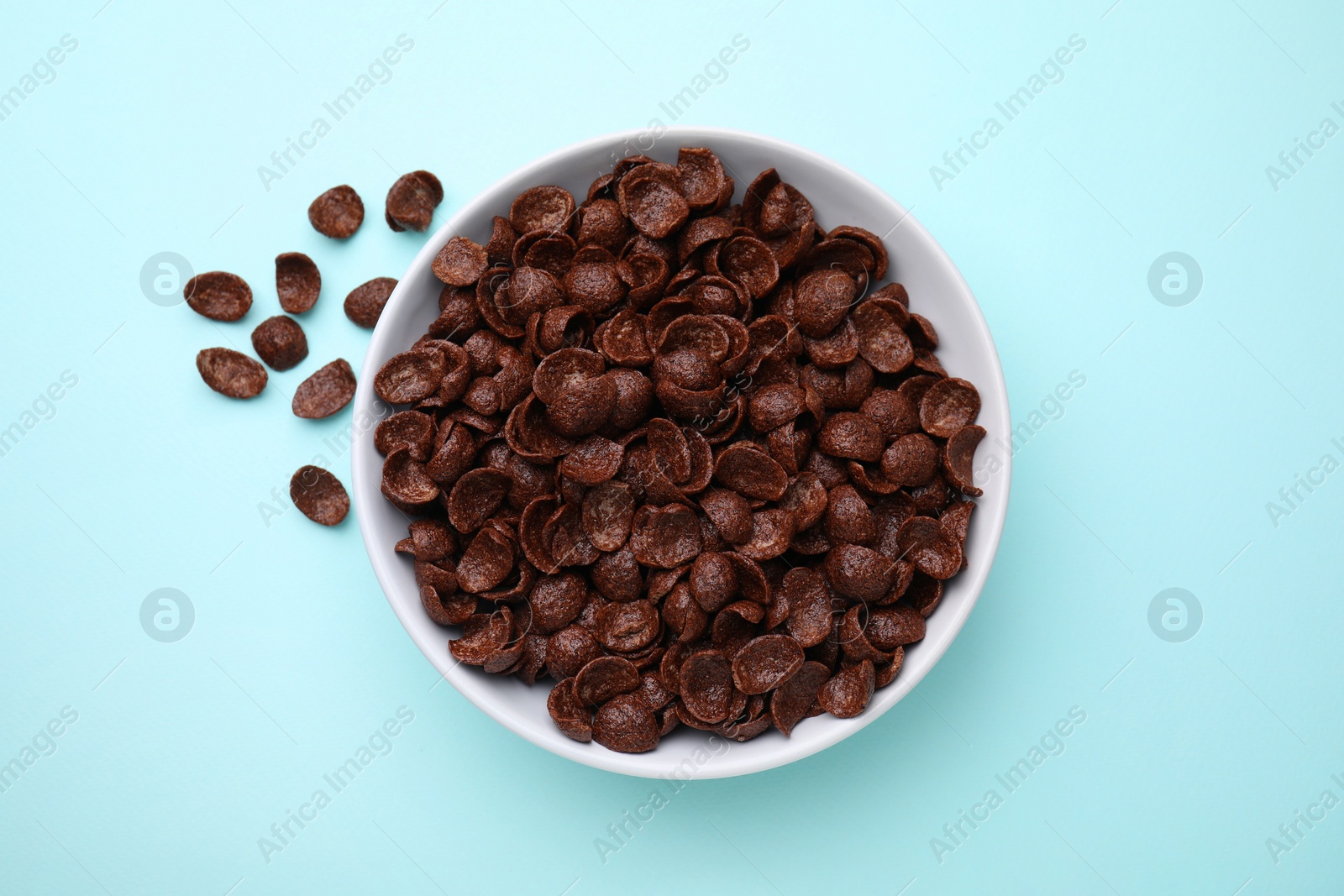 Photo of Breakfast cereal. Chocolate corn flakes in bowl on light blue table, top view