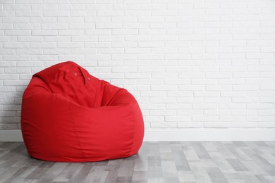Photo of Red bean bag chair near white brick wall in room. Space for text