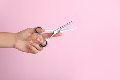 Photo of Hairdresser holding professional thinning scissors and space for text on pink background, closeup. Haircut tool
