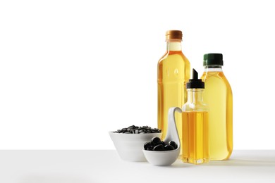 Bottles of different cooking oils, olives and sunflower seeds on white background, space for text