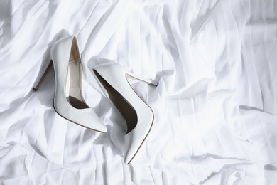 Photo of Pair of wedding high heel shoes on white fabric, above view