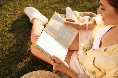 Young woman reading book on green grass near tree in park, above view