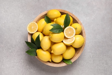 Many fresh ripe lemons with green leaves on light grey table, top view