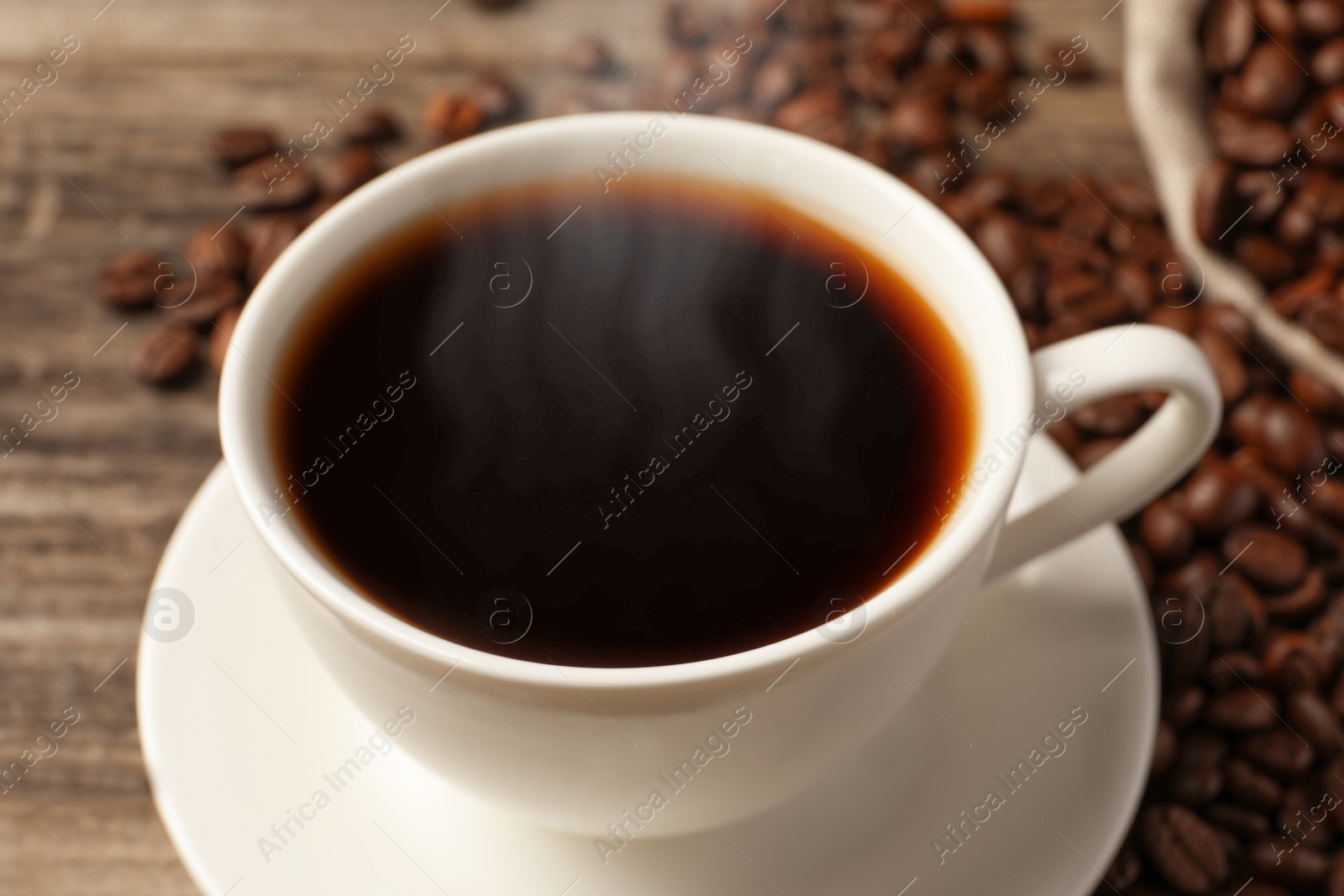 Image of Steaming coffee in cup and roasted beans on wooden table, closeup