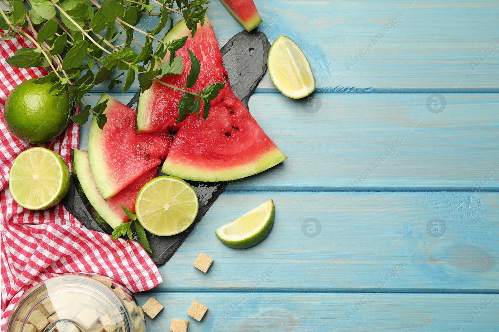 Photo of Cut tasty watermelon served with lime, mint and sugar on light blue wooden table, flat lay. Space for text