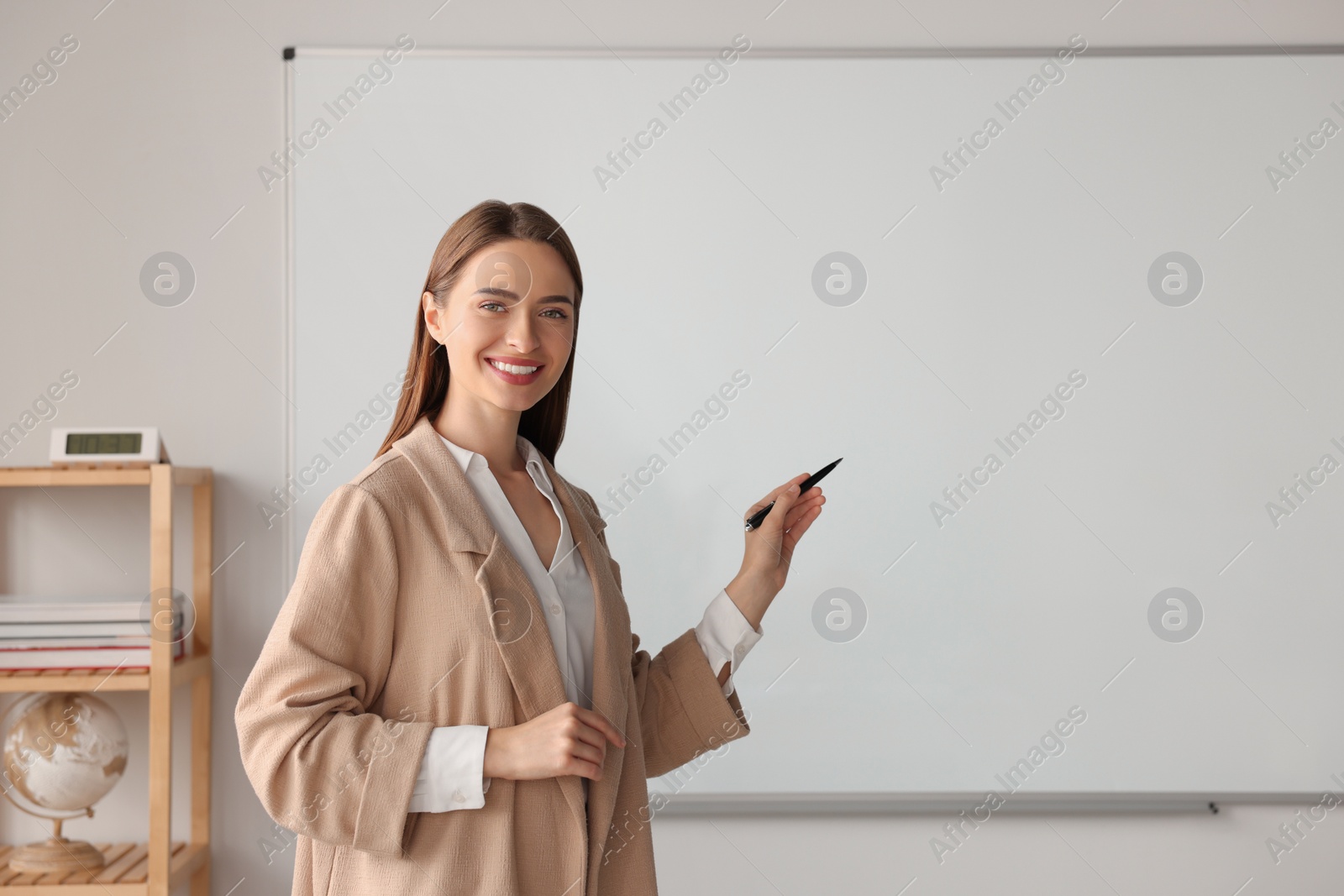 Photo of Happy young teacher explaining something at whiteboard in classroom. Space for text