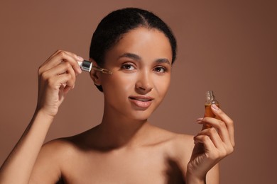 Photo of Beautiful woman applying serum onto her face on brown background