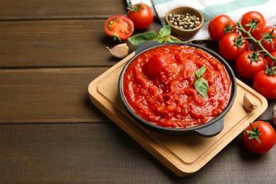 Photo of Homemade tomato sauce in bowl and ingredients on wooden table, space for text