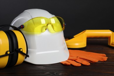 Photo of Hard hat, goggles, earmuffs, suction lifters and protective gloves on wooden surface against gray background