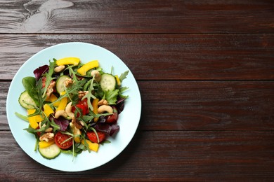 Photo of Tasty fresh vegetarian salad on dark wooden table, top view. Space for text