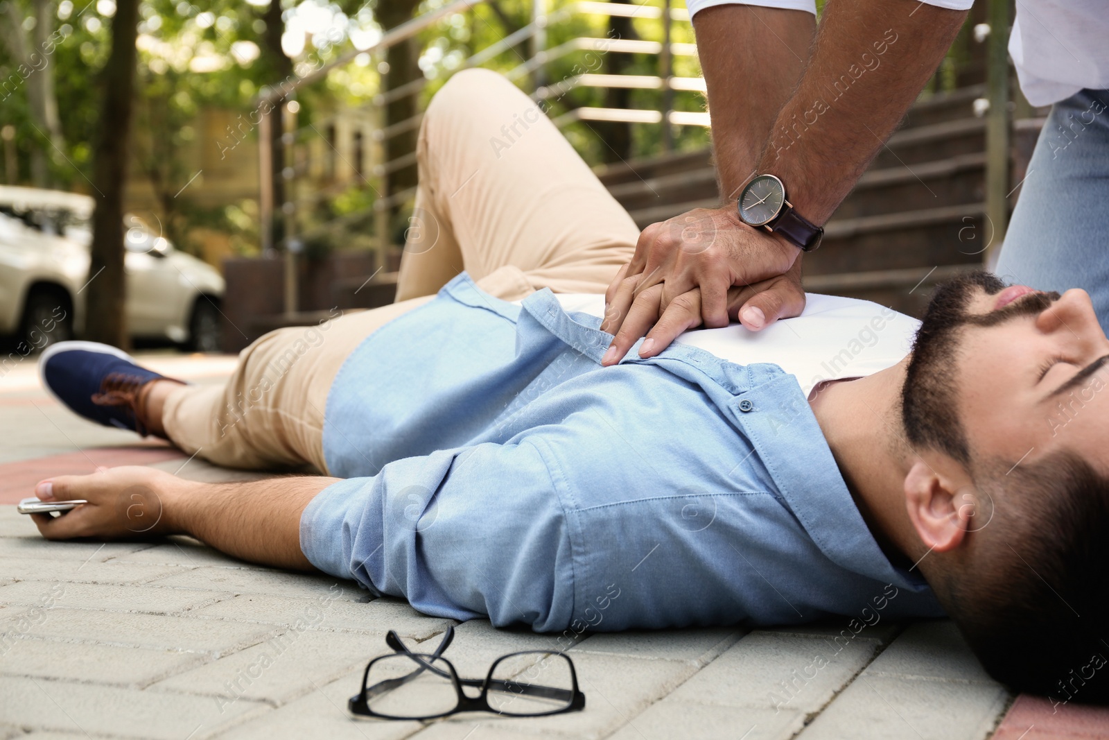 Photo of Passerby performing CPR on unconscious young man outdoors. First aid