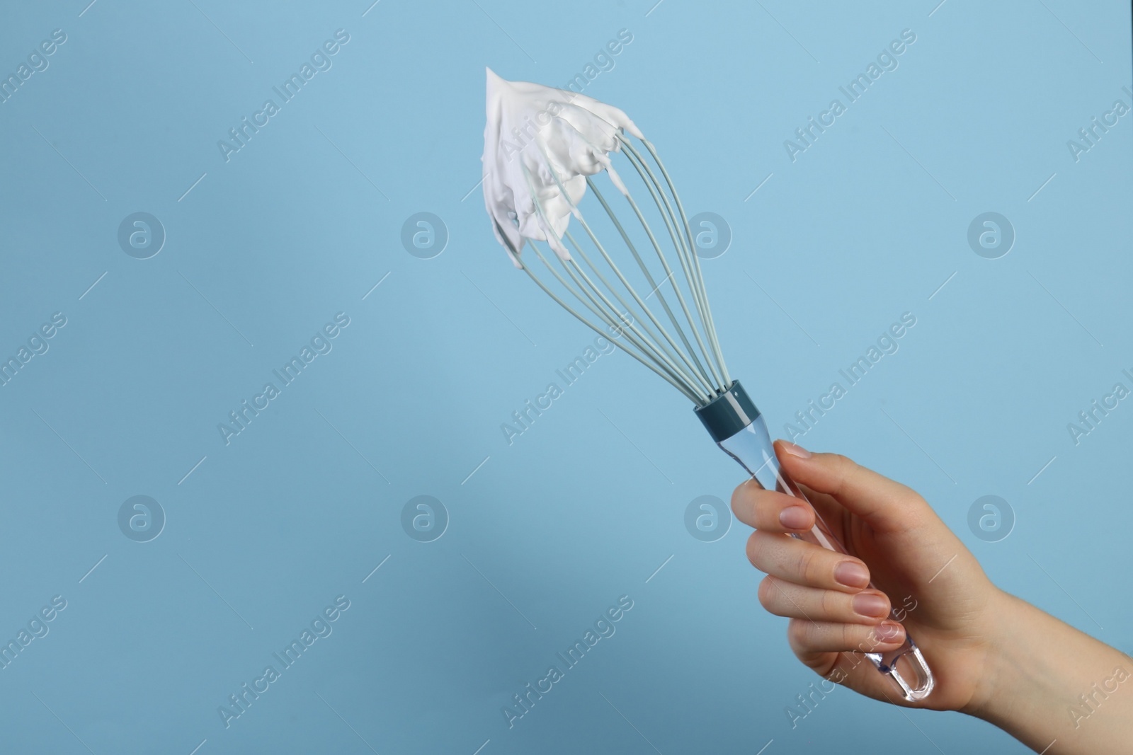 Photo of Woman holding whisk with whipped cream on light blue background, closeup. Space for text