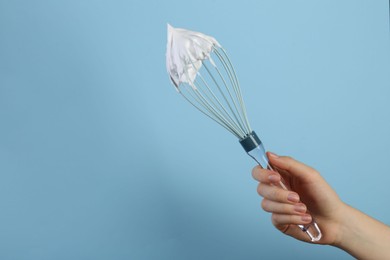 Photo of Woman holding whisk with whipped cream on light blue background, closeup. Space for text