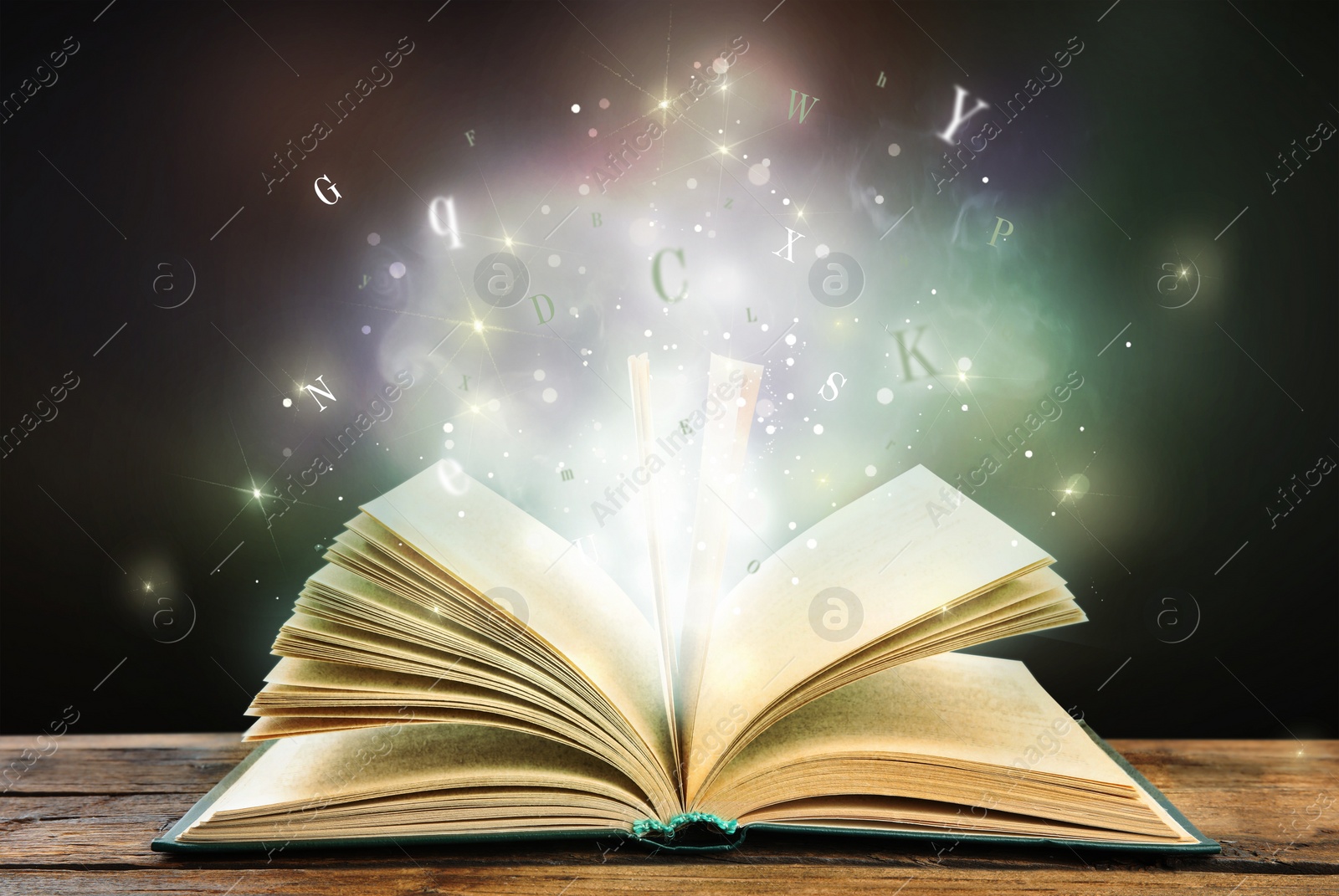 Image of Open book with magic light and glowing letters flying out of it on wooden table against black background