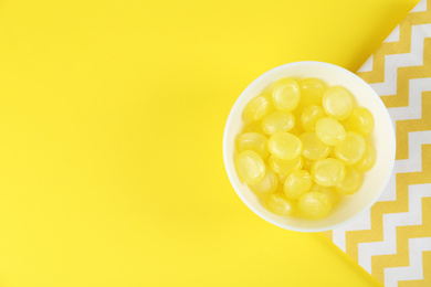 Photo of Delicious lemon drops in bowl on yellow background, flat lay. Space for text