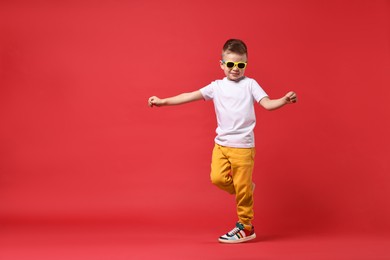 Photo of Happy little boy dancing on red background. Space for text