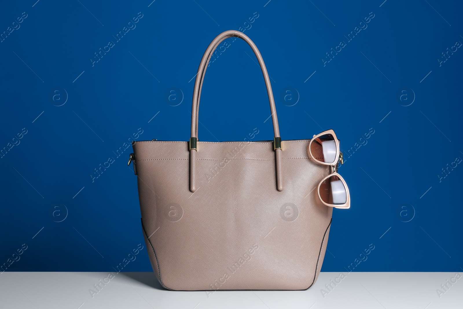 Photo of Stylish woman's bag and sunglasses on white table