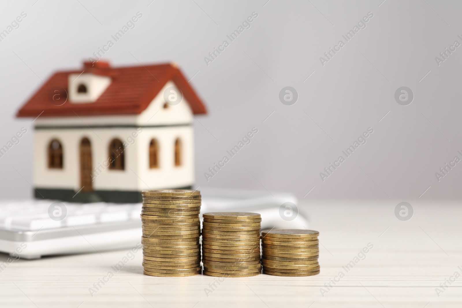 Photo of Mortgage concept. Stacks of coins, model house and calculator on white wooden table, selective focus with space for text