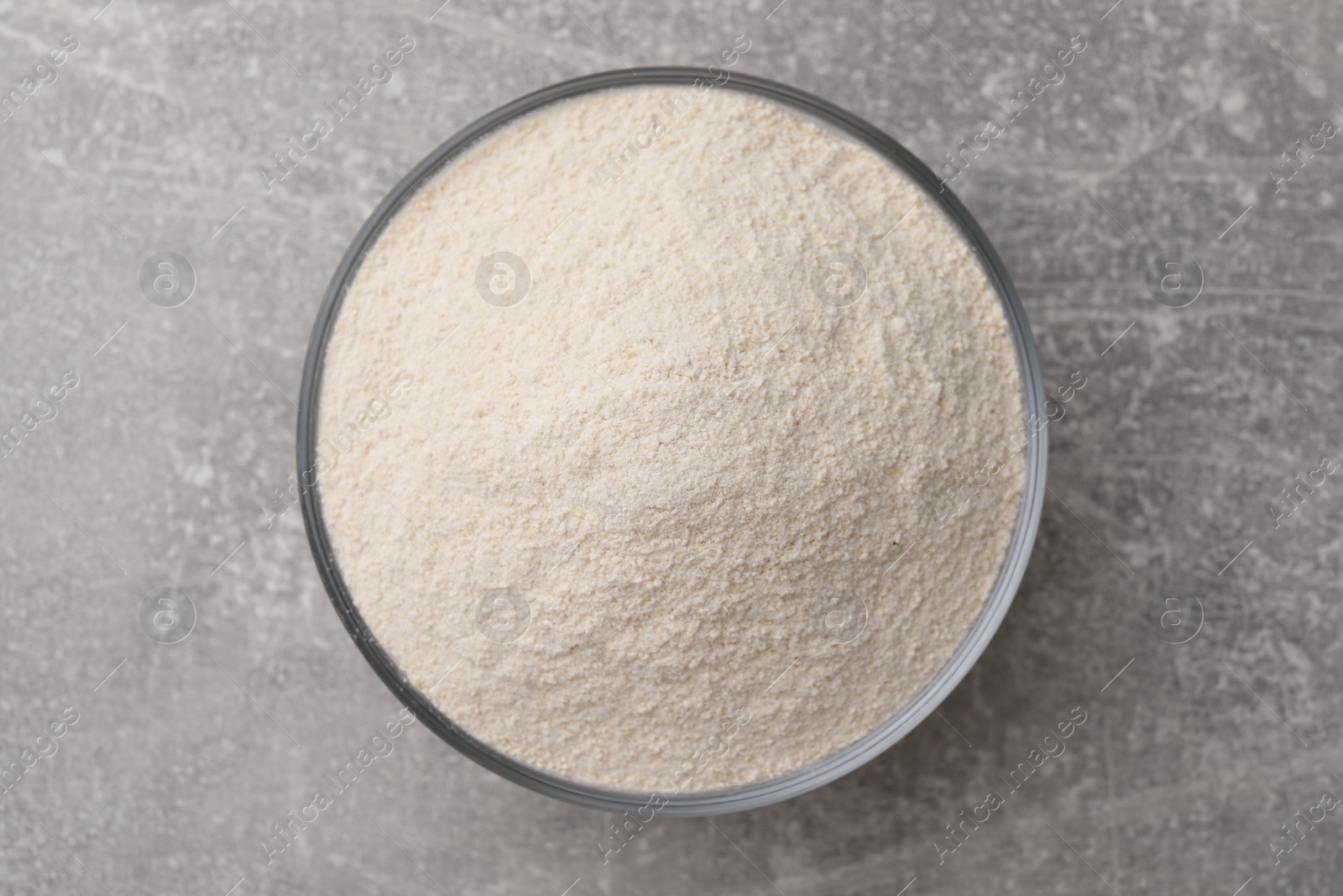 Photo of Glass bowl with quinoa flour on light grey table, top view