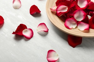 Wooden plate with rose petals on light background, space for text