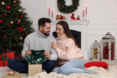 Happy young man opening Christmas gift from his girlfriend at home