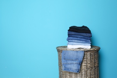 Photo of Stack of different jeans on basket against color wall with space for text