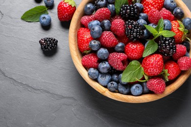 Photo of Many different fresh ripe berries in wooden bowl on black table, flat lay. Space for text