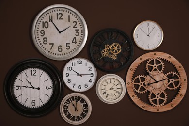 Photo of Collection of stylish clocks on brown wall