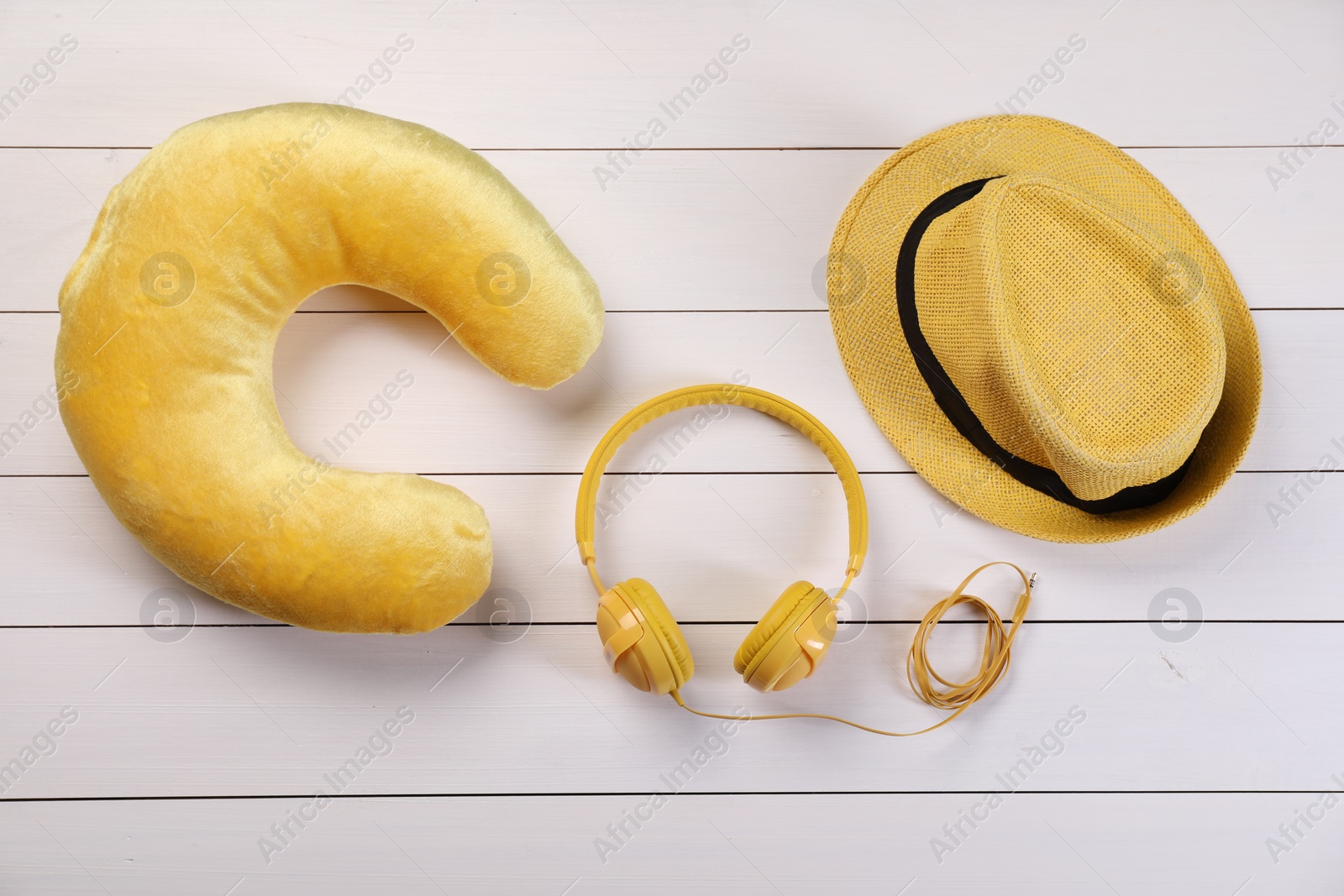 Photo of Yellow travel pillow, hat and headphones on white wooden background, flat lay