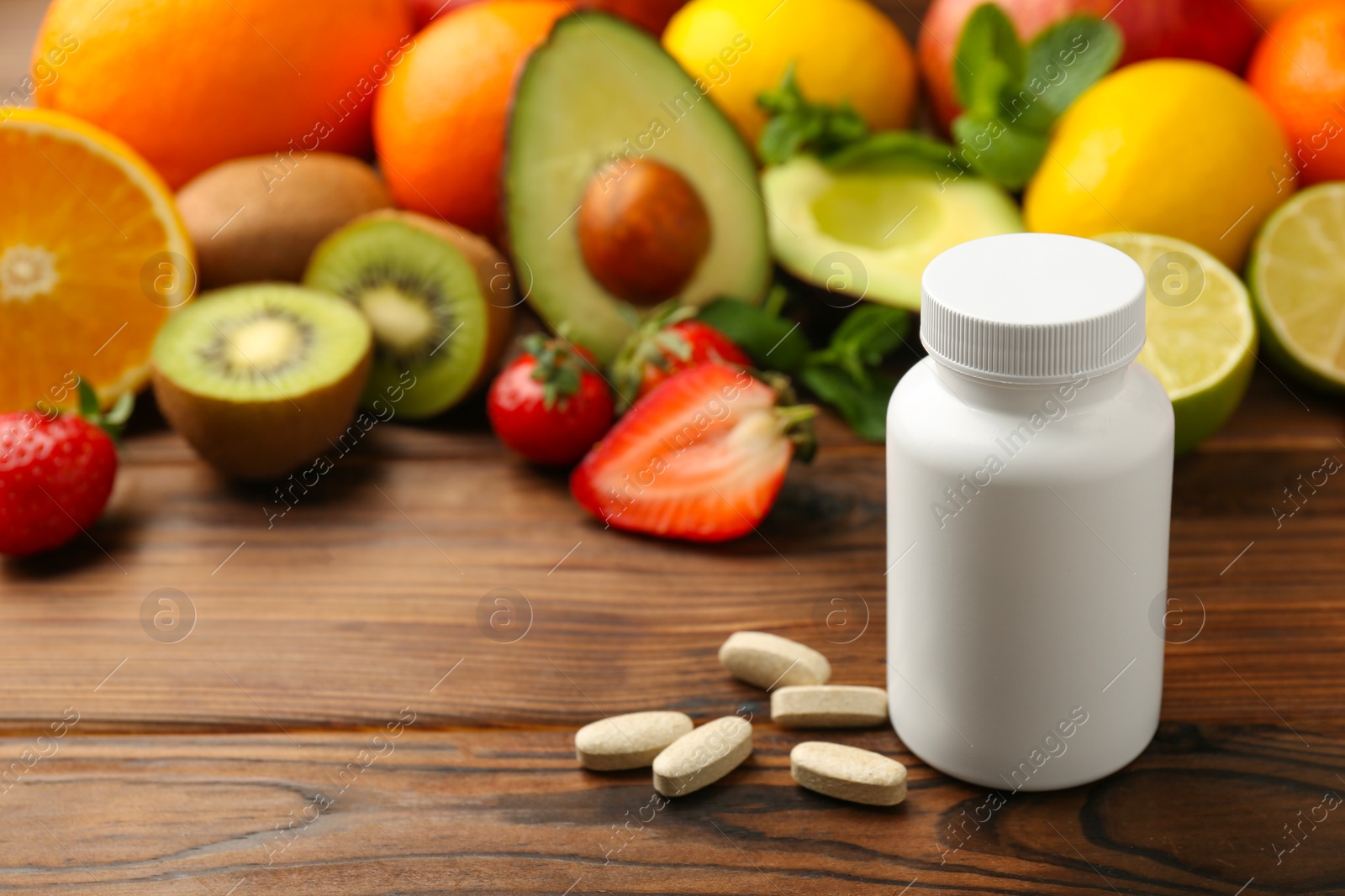 Photo of Vitamin pills, bottle and fresh fruits on wooden table. Space for text