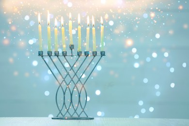 Image of Hanukkah celebration. Menorah with burning candles on table against blurred lights, space for text