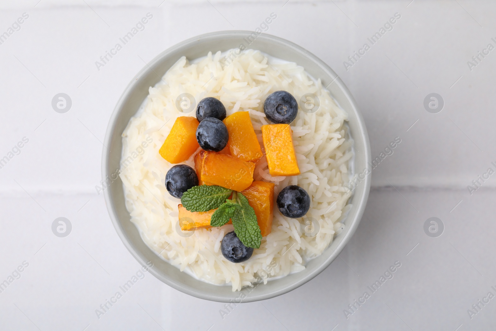 Photo of Bowl of delicious rice porridge with blueberries and pumpkin on white table, top view