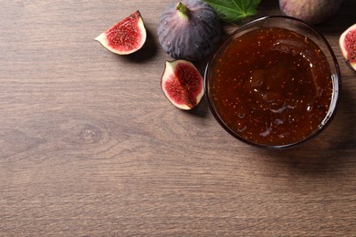 Photo of Glass bowl with tasty sweet jam and fresh figs on wooden table, flat lay. Space for text