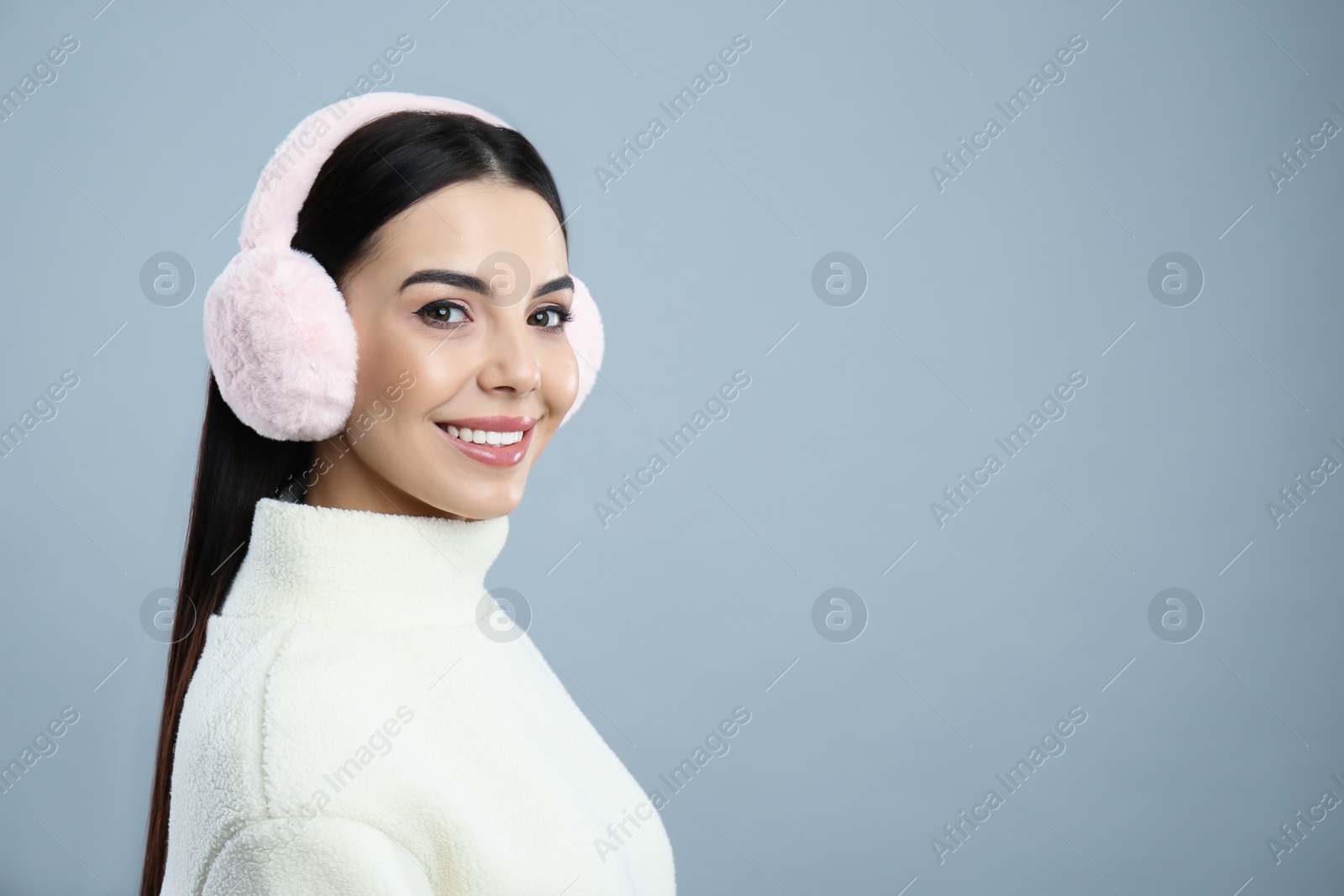 Photo of Beautiful young woman wearing earmuffs on light grey background. Space for text