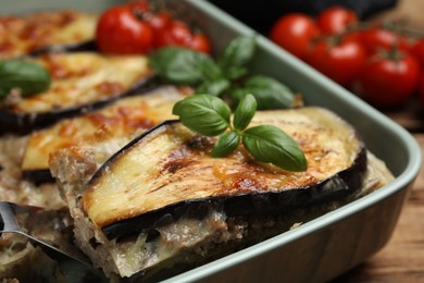 Photo of Spatula with piece of delicious eggplant lasagna over baking dish at table, closeup