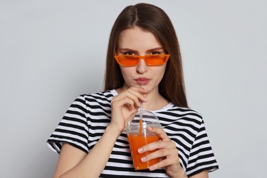 Photo of Beautiful young woman drinking juice from plastic cup on light grey background