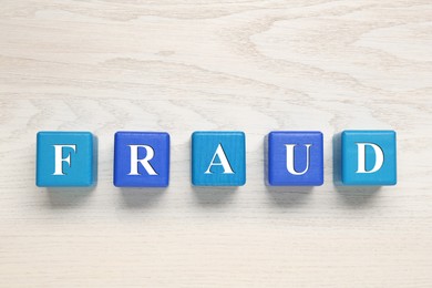 Photo of Word Fraud of cubes with letters on white wooden background, flat lay