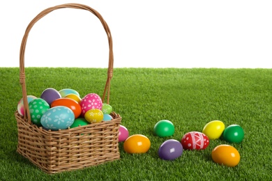 Photo of Wicker basket with Easter eggs on green grass against white background. Space for text