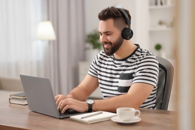 Young man in headphones watching webinar at table in room