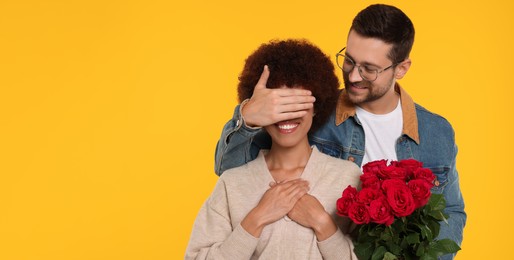 Photo of International dating. Handsome man presenting roses to his beloved woman on orange background