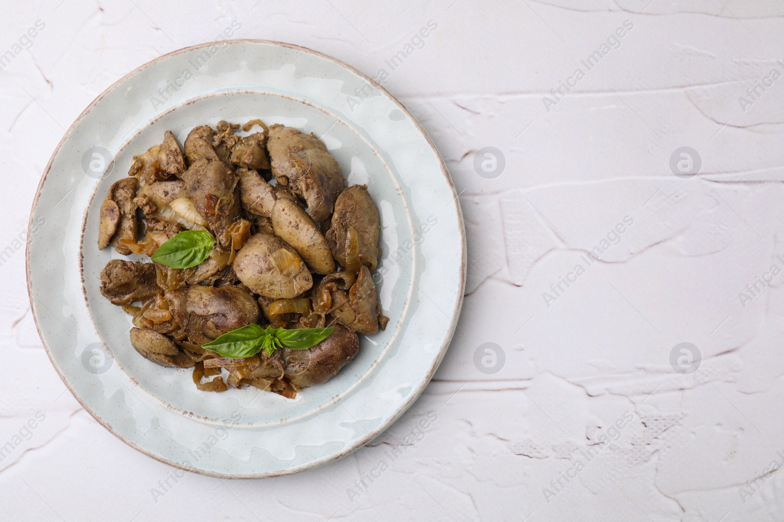 Photo of Plate of delicious fried chicken liver with onion and basil on white textured table, top view. Space for text