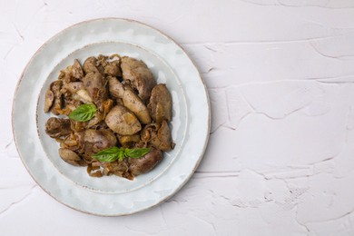 Photo of Plate of delicious fried chicken liver with onion and basil on white textured table, top view. Space for text