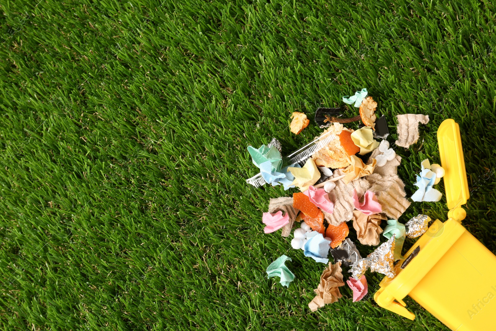 Photo of Trash bin and different garbage on green grass, top view with space for text. Waste recycling concept