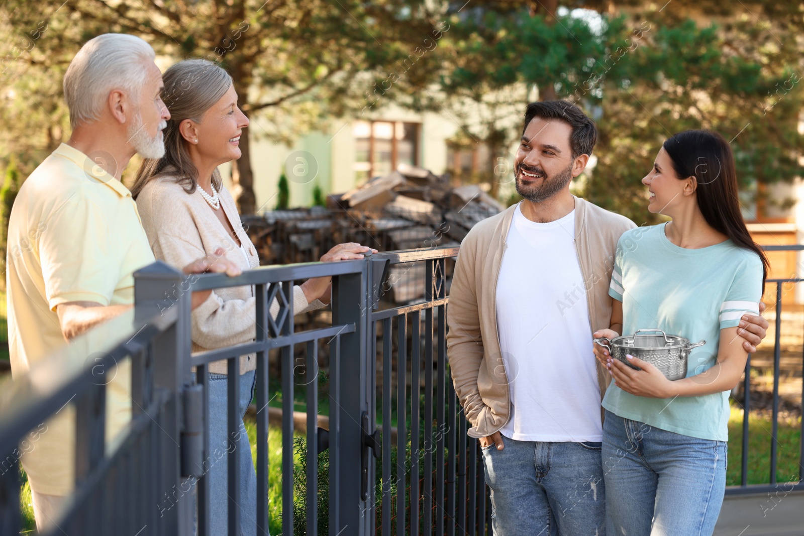 Photo of Friendly relationship with neighbours. Young family talking to elderly couple near fence outdoors