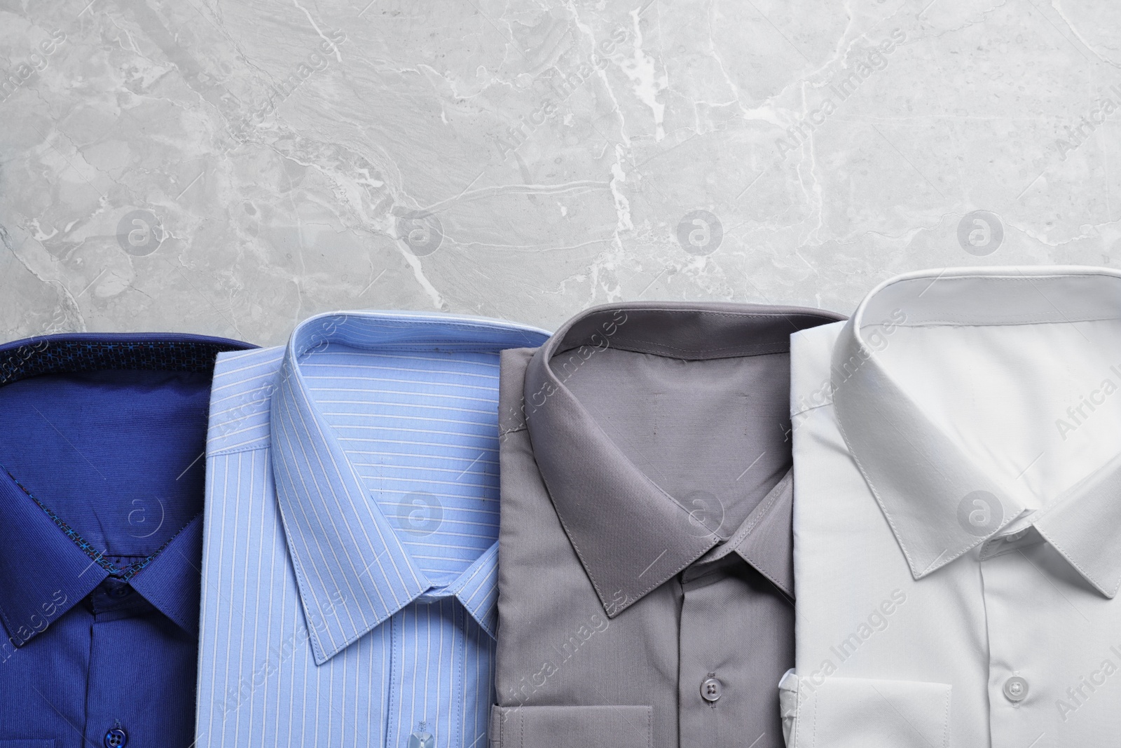 Photo of Stylish shirts on grey marble table, flat lay with space for text. Dry-cleaning service