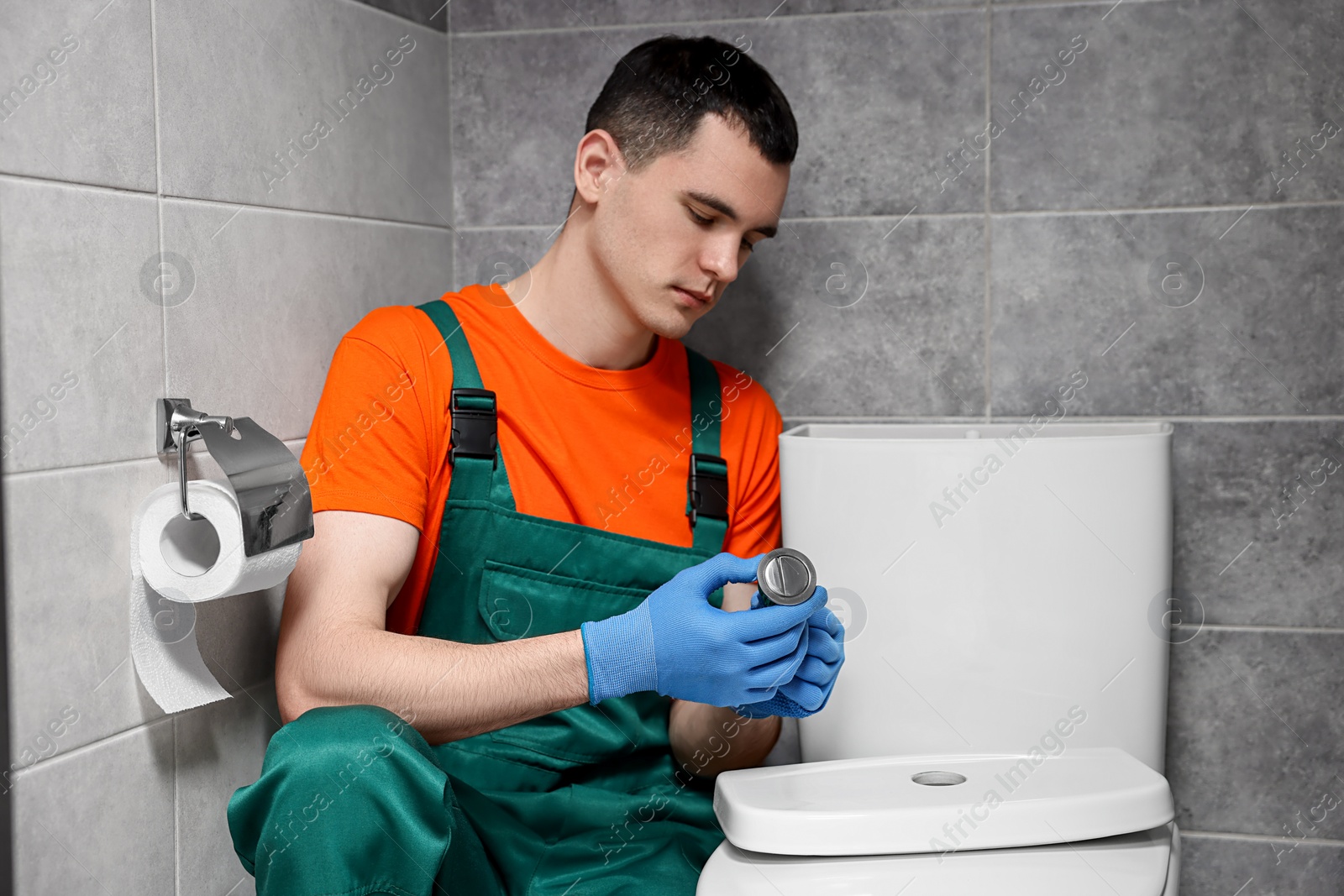 Photo of Young plumber repairing toilet bowl in water closet