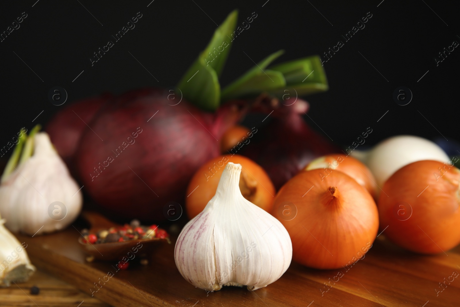 Photo of Fresh onion bulbs, leek, garlic and peppers mix on wooden table, closeup